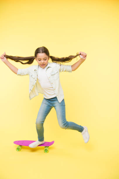 istock Active leisure concept. Kid having fun with penny board. Child smiling face stand on skateboard. Penny board cute colorful skateboard for girls. Lets ride. Girl ride penny board yellow background 1296719881