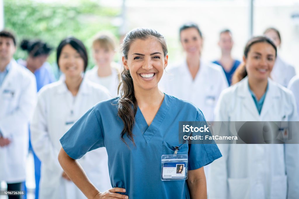 Successful journey through medical school A female medical student of Hispanic ethnicity smiles for the camera as she stands in front of her group of medical professionals in the background. Healthcare And Medicine Stock Photo
