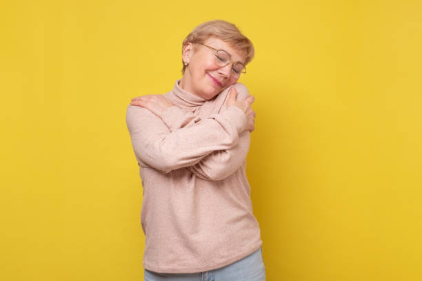 Joyful elderly mature lady closing eyes and embracing herself.