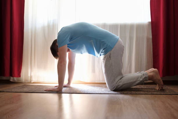 man practices yoga asana marjariasana or cow pose at home. Young man practices yoga asana marjariasana or cow pose at home. cat pose yoga stock pictures, royalty-free photos & images