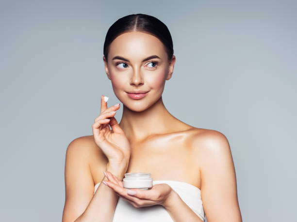 istock Cute woman applying cream to her face 1296731042