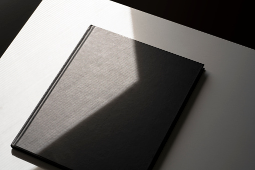 Black blank magazine, book cover mockup, template at the corner of the table with natural light and shadow