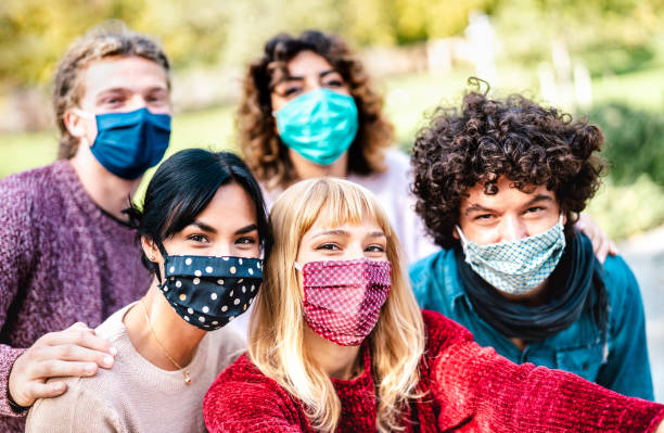 istock Multiracial people taking selfie wearing face mask and spring clothes - New normal lifestyle concept with young friends having fun together outside - Bright filter with focus on central blond girl 1296733593