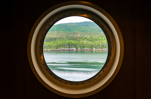 Porthole window view along the Inside Passage cruise, Vancouver island, British Columbia, Canada. Focus on landscape.
