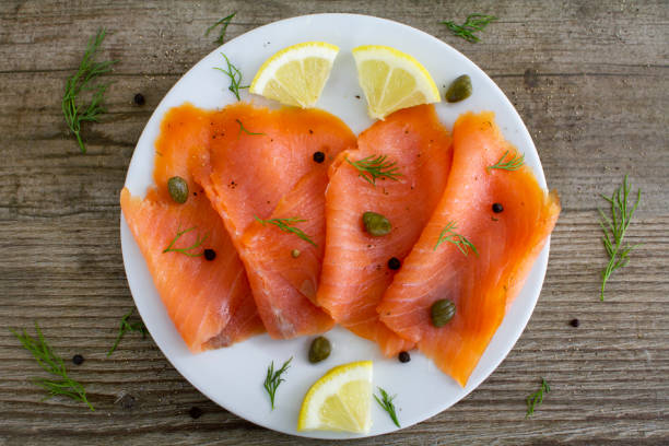 Smoked salmon slices with capers and dill Fresh smoked salmon on a white plate with lemon, capers, black pepper and dill. 
Shot from above on a rustic table. Close up. smoked salmon stock pictures, royalty-free photos & images