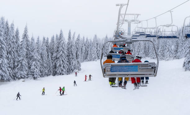 los esquiadores montan en el teleférico mientras otros esquiadores esquian por la montaña - telesilla fotografías e imágenes de stock