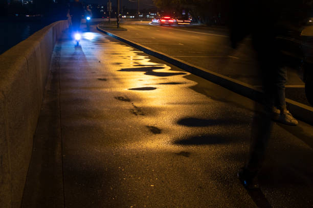 istock Wet sidewalk with puddles at night. Bicyclists use warning front blue light for safety reason. Selective focus. 1296742503