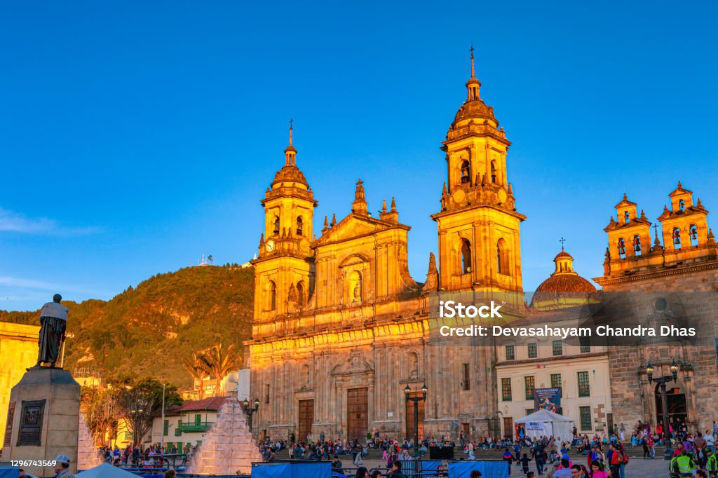Bogota, Colombia - The North Eastern Corner of Plaza Bolivar In The Andean Capital City; The Upper Half Of The Ninteenth Century Catedral Primada, Is Turned To Gold By The Setting Sun. Looking from Plaza Bolivar, in the Andean Capital city of Bogota, in Colombia, South America, to the North Eastern corner of the Square. The 19th Century Catedral Primada has the upper half turned to gold by the setting sun. The Cathedral is the seat of the Roman Catholic Archbishop of Colombia. A few metres to the right, is the Archbishop's chapel. A section of his palace can also be seen. The style of architecture is classical colonial Spanish. In the far background is the mountain peak of Monserrate. The altitude at street level is about 8,500 feet above mean sea level. Image shot in the late afternoon sunlight; horizontal format. Copy space. Bogota Stock Photo