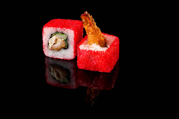 istock Two red tuna rolls with red caviar and shrimp on a black background with reflection. Close-up, top view. Food delivery concept. 1296744967