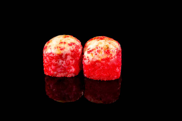 istock Two red tuna rolls with red caviar and shrimp on a black background with reflection. Close-up, top view. Food delivery concept. 1296745018