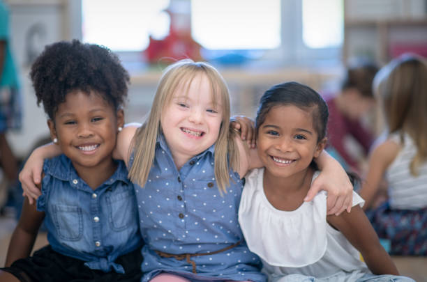 Best friends in preschool Three multi ethnic preschool girls in their classroom. One of the girls (in the middle) is of Caucasian ethnicity and has Down syndrome. The other girls are of African and mixed race ethnicity. disability stock pictures, royalty-free photos & images