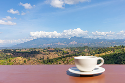 Mountainous tropical landscape view background with a blurred cup of coffee on a balcony as foreground