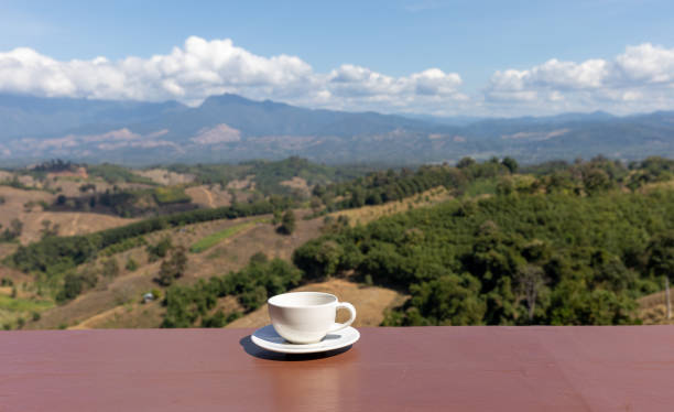 A cup of coffee on a balcony with blurred mountainous tropical landscape view as background