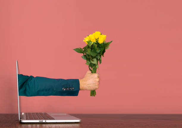 mano che esce da un laptop con rose gialle in mano. concetto covid di san valentino. - appears foto e immagini stock