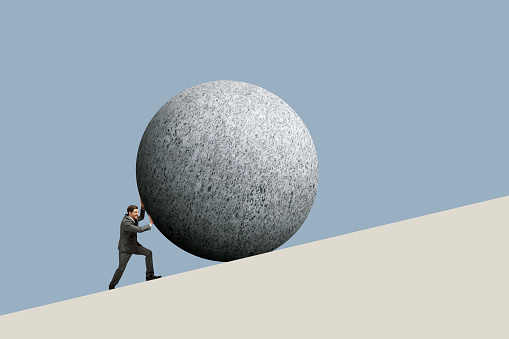 A businessman attempts to push a large stone sphere up a hill.