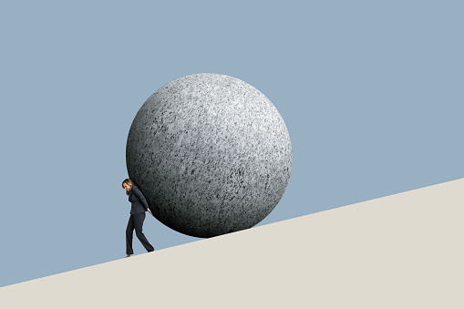 A businesswoman attempts to push a large stone sphere up a hill.