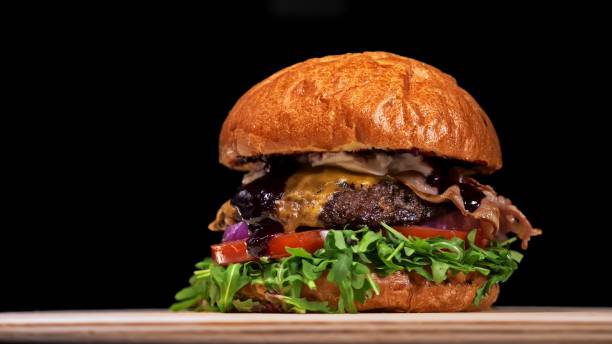 istock Craft burger is cooking on black background. Consist: sauce, arugula, tomato, onion, bacon, currant sauce, ricotta cheese, air bun and marble meat. 1296787197