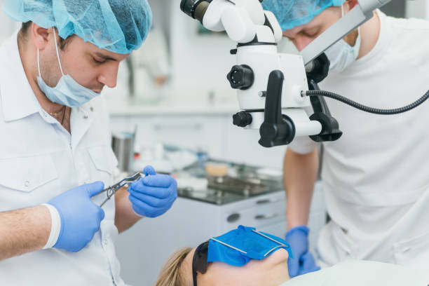 istock Doctor used microscope. Dentist is treating patient in modern dental office. Operation is carried out using cofferdam. Client is inserted and restored teeth, make denture. 1296787967