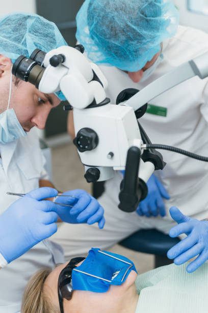 istock Doctor used microscope. Dentist is treating patient in modern dental office. Operation is carried out using cofferdam. Client is inserted and restored teeth, make denture. 1296787979