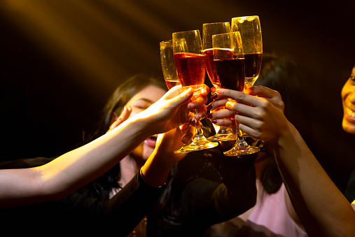 Group of people toast drinks at party in dancing club at night . Social gathering event and nightlife entertainment concept .