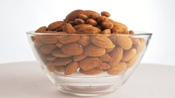 istock Nuts almond rotate are on a table in a plate. Snack in transparent dish on an isolated white background are spinning moving. 1296789152