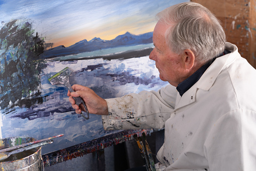 Mature male artist painting impressionistic abstract art in his studio.
