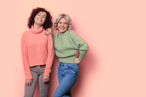 Monochrome photo of two women with curly hair posing on a studio wall with free space smiling at camera