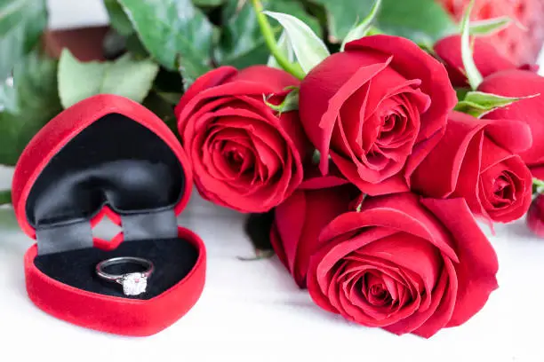 Red rose bouquet and red box with engagement ring on white background.