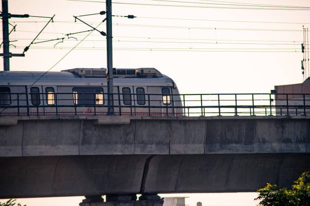 Jaipur, Delhi, India - circa 2021 : Aerial dusk shots of metro train on elevated bridge with people visible through transparent windows and wires and support visible. Shows the restarting of the public transport commute option as offices open up after the COVID19 coronavirus pandemic