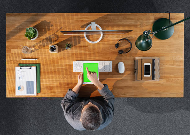 istock Top view of businessman working on computer at desk with keyable screen in home office. 1296812202