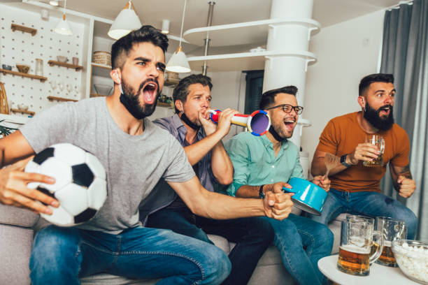 glückliche männliche freunde, die zu hause fußball schauen - sitting 20s adult american football stock-fotos und bilder