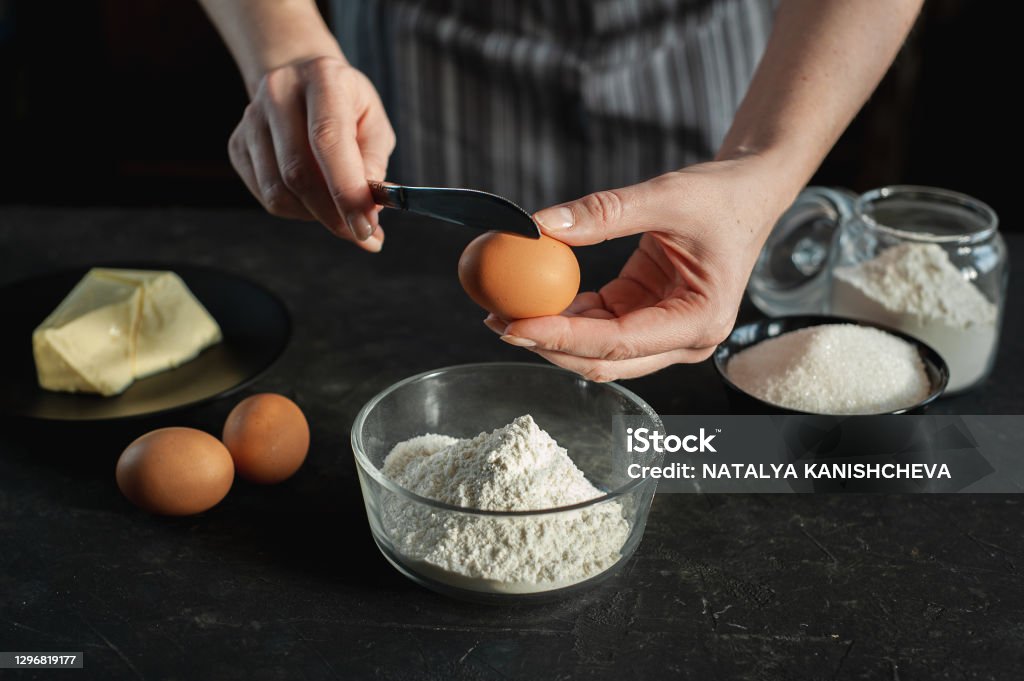 반죽을 준비하는 과정 여자는 계란을 깨고 밀가루 그릇에 추가합니다 여성의 손에 계란과 칼 어두운 배경에 반죽재료 갈색에 대한 ...