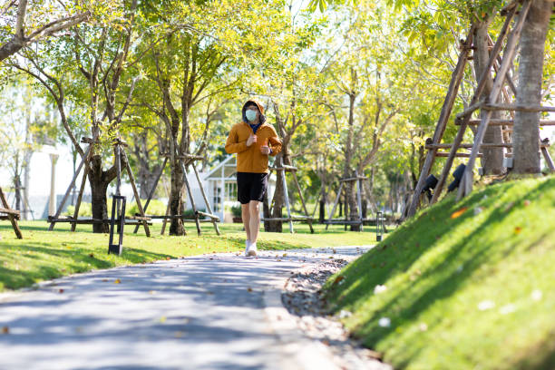 istock Asian Man in yellow hoodie  wearing protective face mask doing stretching exercise beside railway in park at autumn morning. 1296821302
