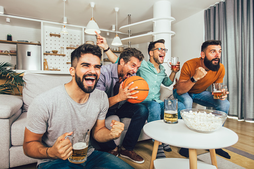 Happy friends or basketball fans watching basketball game on tv and celebrating victory at home.