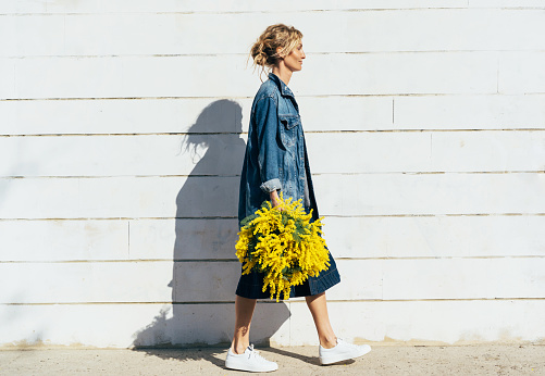 Stylish young woman in denim clothes with a bouquet of mimosa