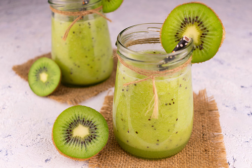 Two healthy fresh kiwi  smoothies in jars on a gray background.