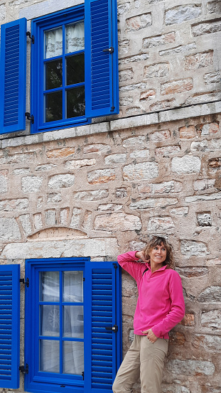 Woman in red polar near stone house with blue windows. Bodrum travel.