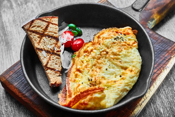 omelet with tomatoes and white onions in a black pan and a slice of rye bread. Healthy breakfast with your own hands. Delicious coffee with cane sugar stock photo