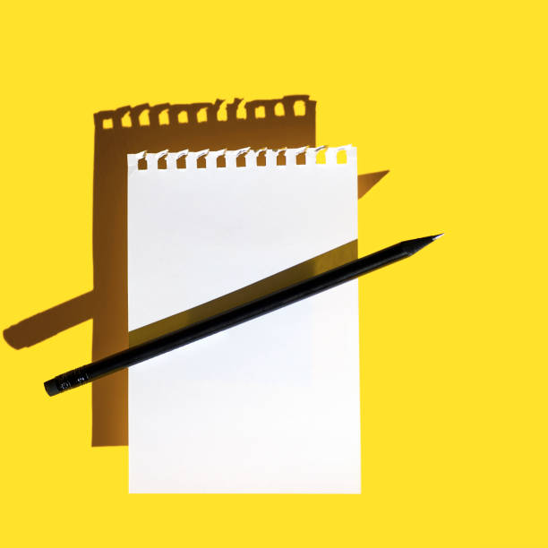 istock a blank sheet of Notepad, black pencil and hard shadows on bright yellow background 1296827408