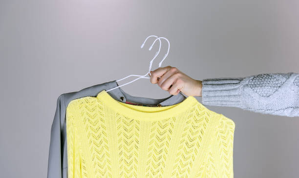 istock Woman holding grey and yellow sweaters on hangers. 1296832929