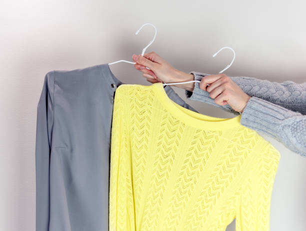istock Woman holding grey and yellow sweaters on hangers. 1296833003