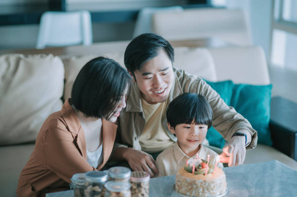 asian chinese father igniting birthday candle with lighter getting ready to sing birthday song for their son in living room celebrating birthday