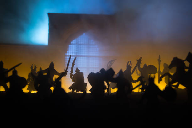 istock Medieval battle scene with cavalry and infantry. Silhouettes of figures as separate objects, fight between warriors on sunset foggy background. 1296837624