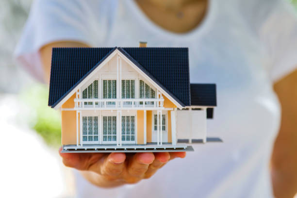 Cheerful blonde Real Estate Agent standing in an empty room presenting a mini model house