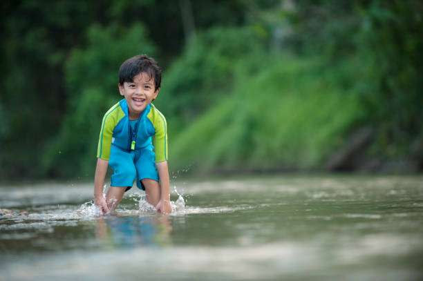 Asian kids playing by the river with turquoise swimming suit and bending his knee inside the water.