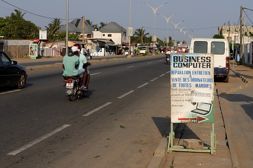 Avepozo, Togo - November 30, 2019: Shop advertisment with a painted picture on the highway. The shop sells computers and people repair computer. Location: Avepozo, Togo, West Africa. A motorbike taxi passes the sign.