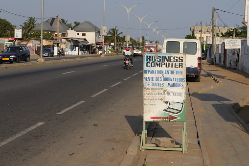 Avepozo, Togo - November 30, 2019: Shop advertisment with a painted picture on the highway. The shop sells computers and people repair computer. Location: Avepozo, Togo, West Africa. A motorbike taxi passes the sign.