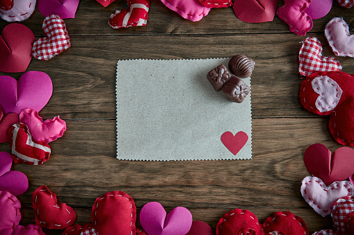 Valentine's Day theme: Red and pink hearts with blank cardboard on a wooden table forming a frame with copy space