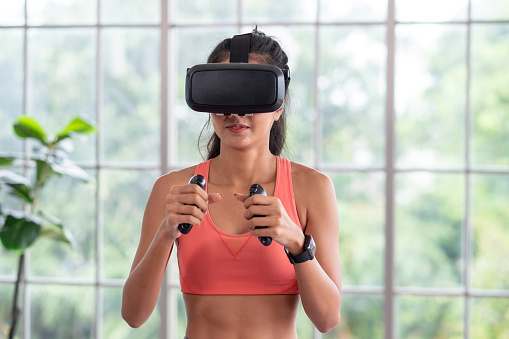 Asian woman wear virtual reality glasses and train boxing with joystick control at home,Future technology for fitness lifestyle concept.