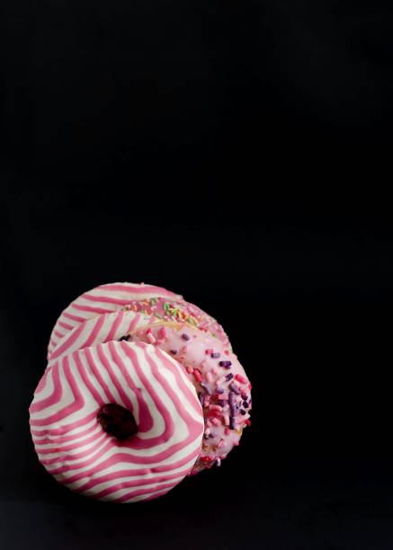 istock Donuts with pink icing on black background with copy space and flat lay 1296854974